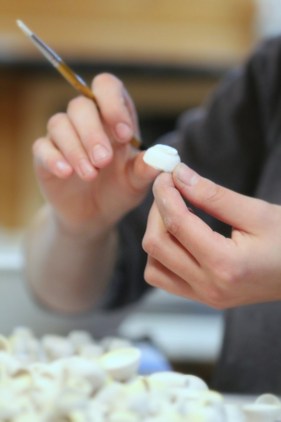 Hands carefully paint a small white sculpture in a workshop.