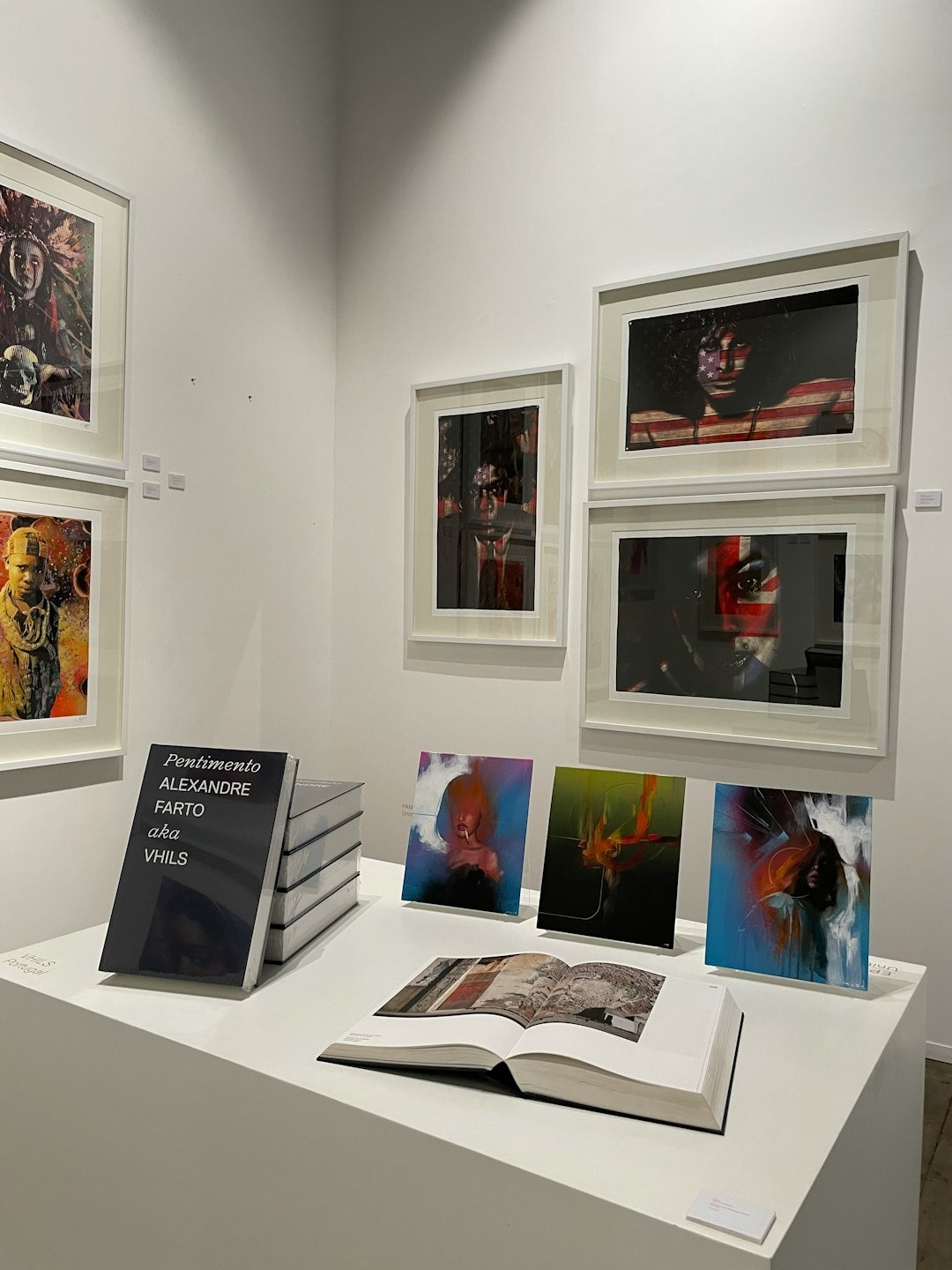Art gallery exhibition featuring framed portraits and stacked books on pedestals.