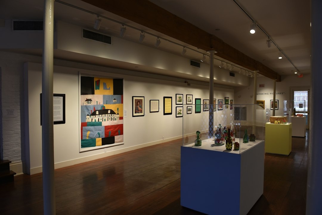 Quilted wall art and framed paintings displayed in an art gallery.